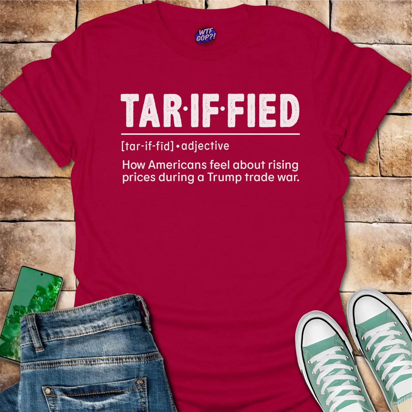 Red t-shirt with 'TAR-IF-FIED' text on a brick surface with jeans and sneakers.