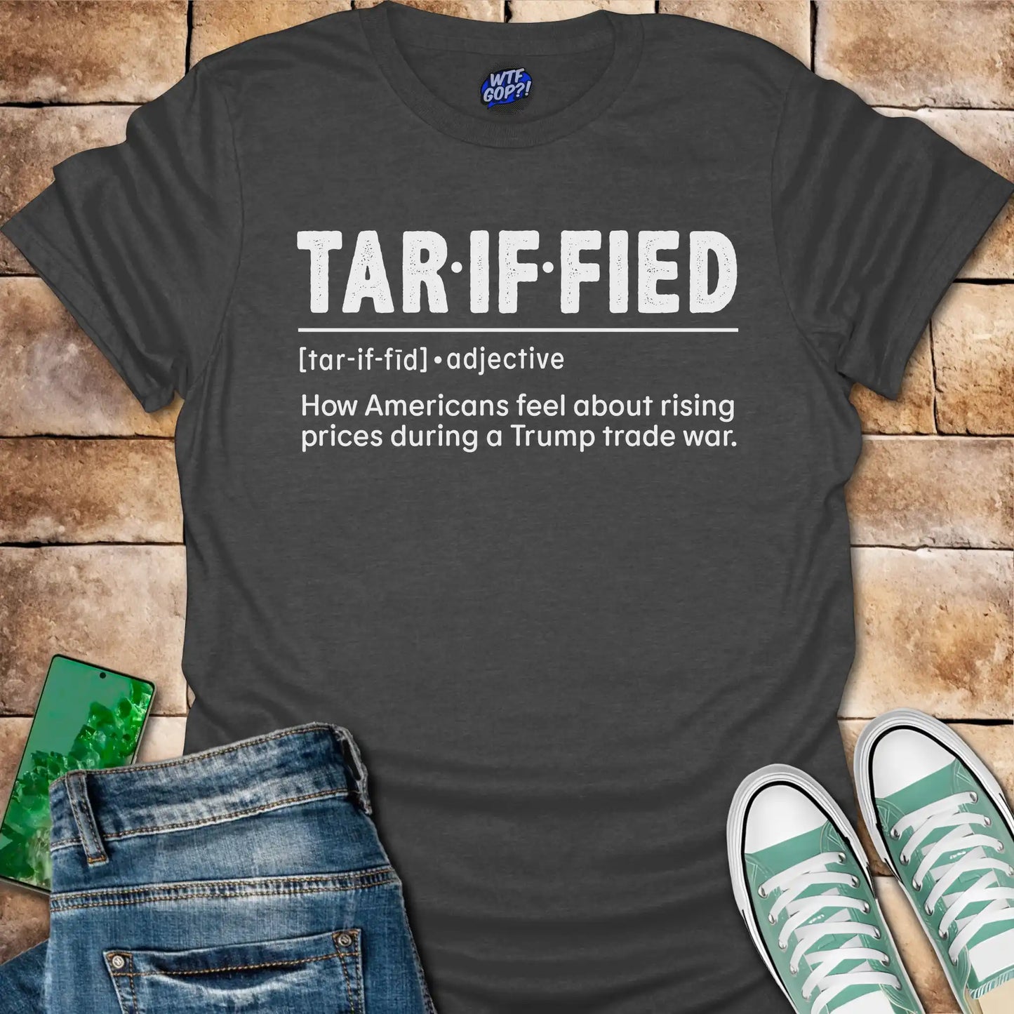 Dark gray t-shirt with 'Tariffied' text on a brick surface with jeans and sneakers.