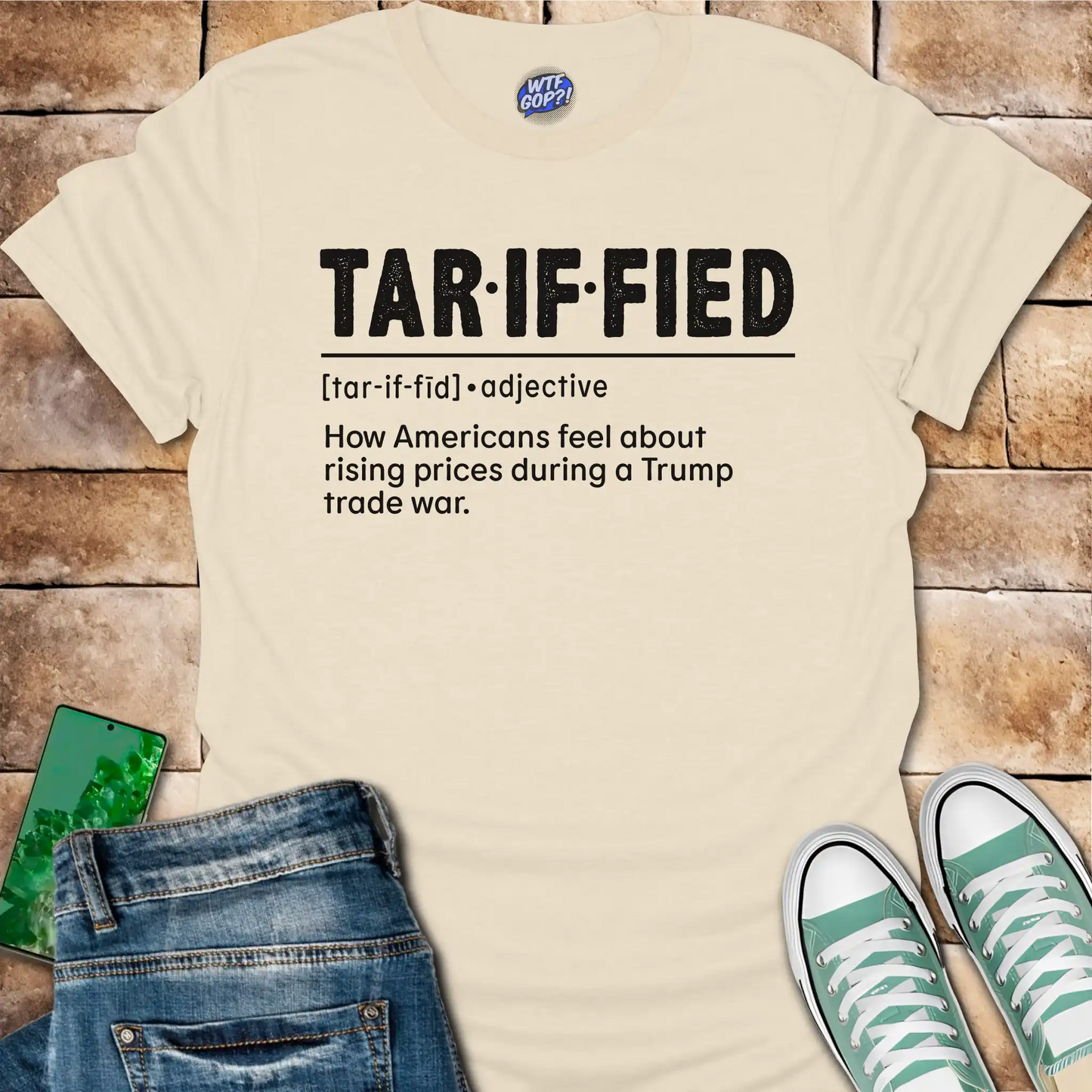 Natrual t-shirt with text 'TAR-IF-FIED' on a brick surface with jeans and shoes.