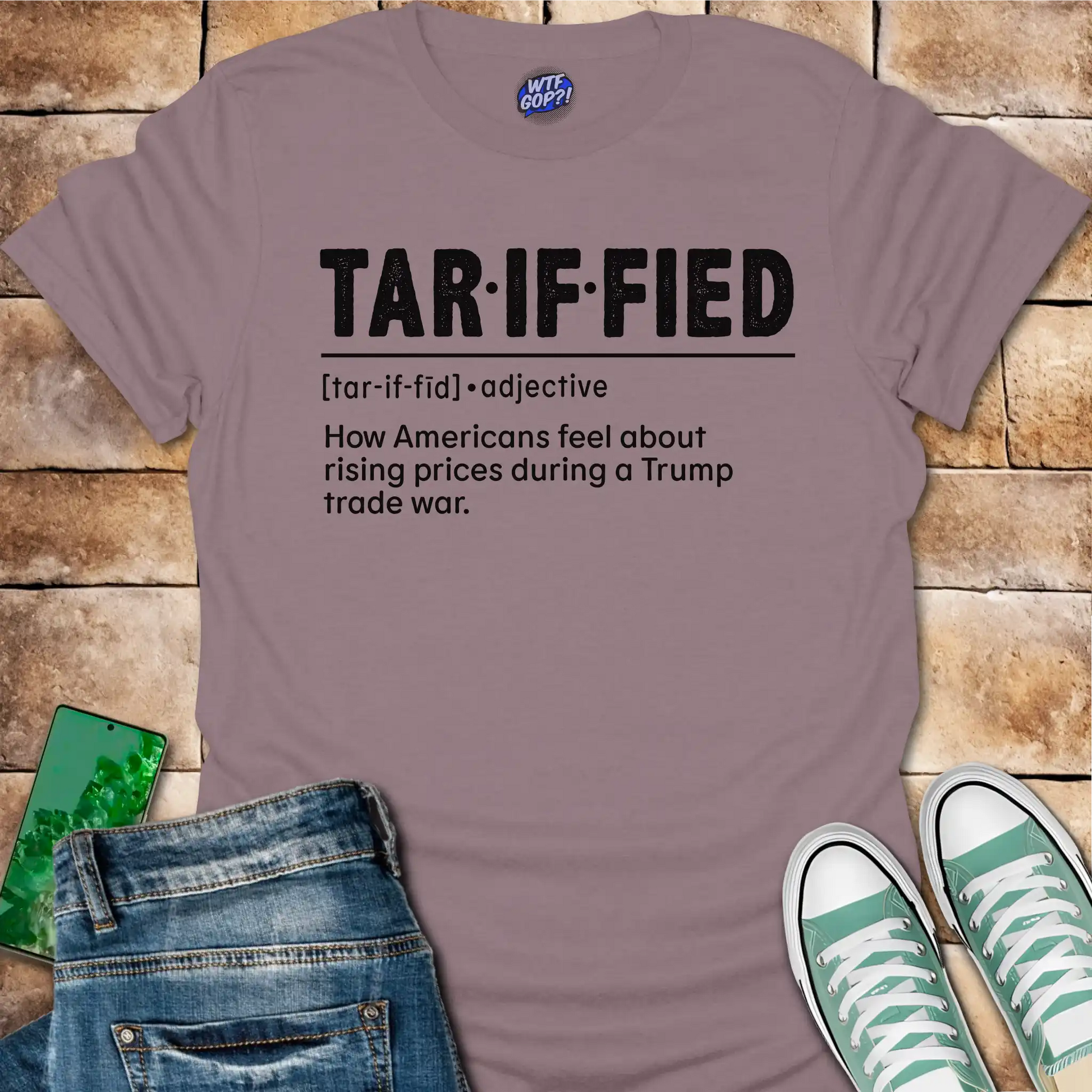 Mauve t-shirt with 'TAR-IF-FIED' text on a wooden surface with jeans and sneakers.