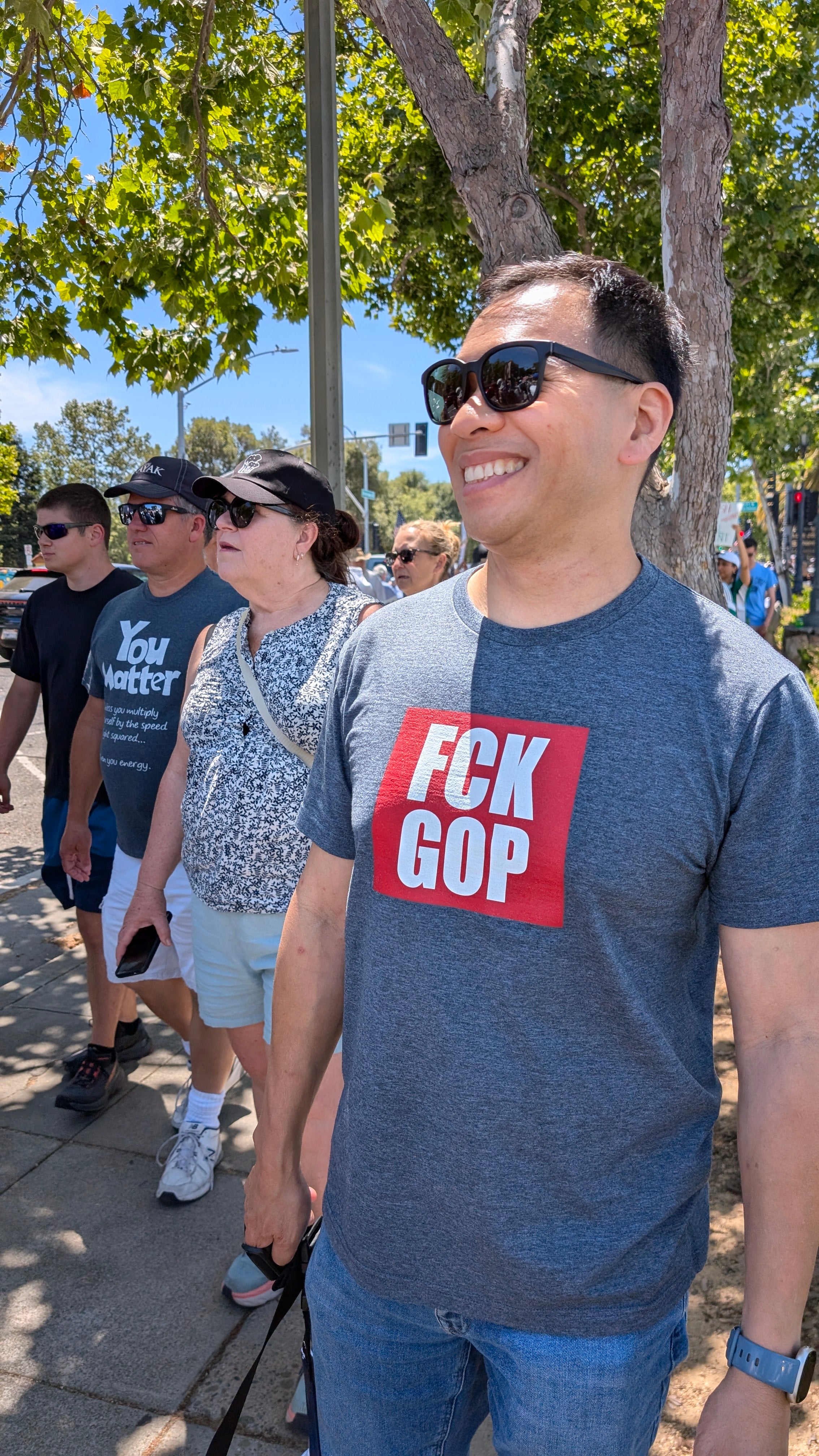 Man wearing a blue t-shirt with 'FCK GOP' printed on it, walking outdoors.